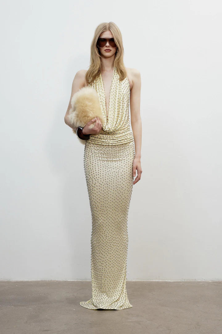 Woman in a long, patterned dress holding a fur stole against a plain background